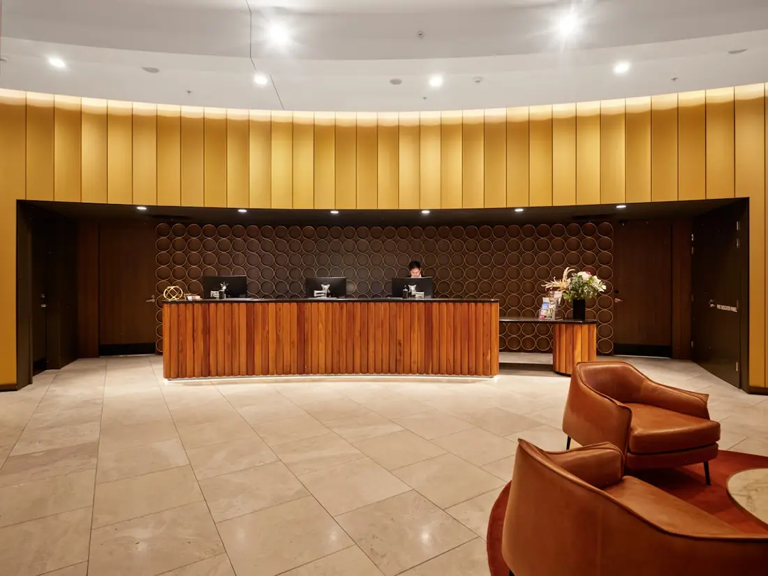 An empty hotel reception desk in warm wood, seating beyond it